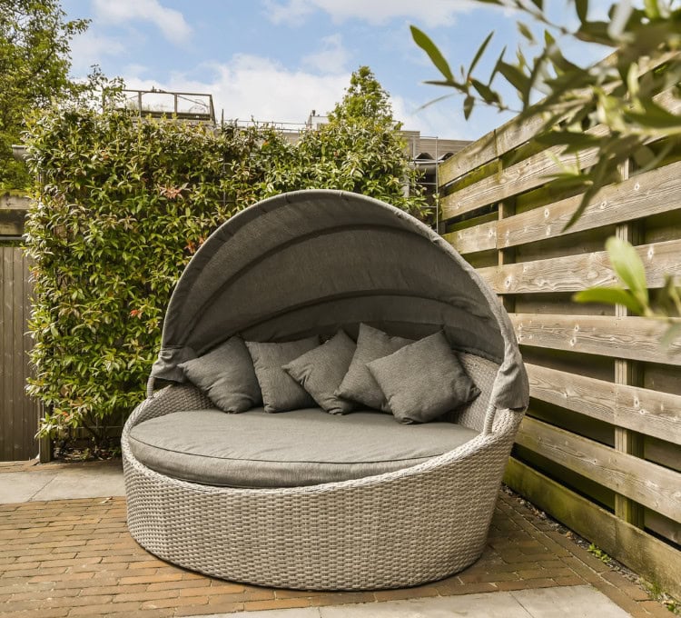 Comfortable outdoor wicker daybed with canopy and cushions, perfect for relaxation and lounging in the garden.