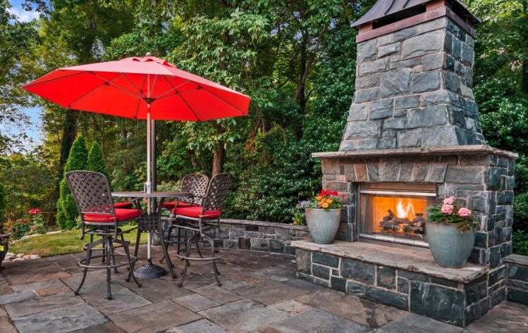 Cozy outdoor patio with a fire fireplace, red umbrella, and seating area perfect for relaxing in a beautiful backyard setting.