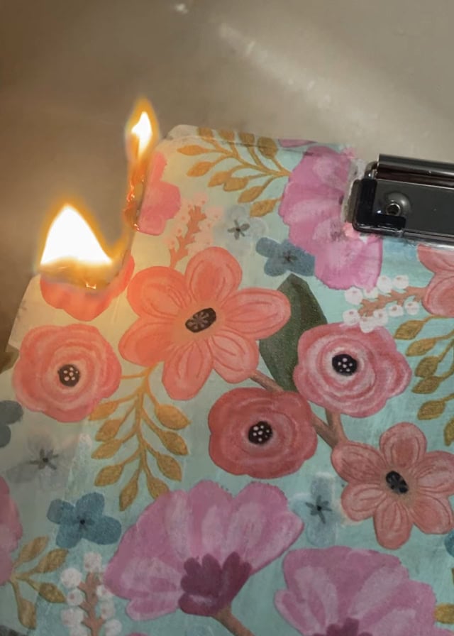 Fire starts on floral watercolor-patterned paper, creating a small blaze with visible flames and melted edges, close-up of the burn process on decorative art material.