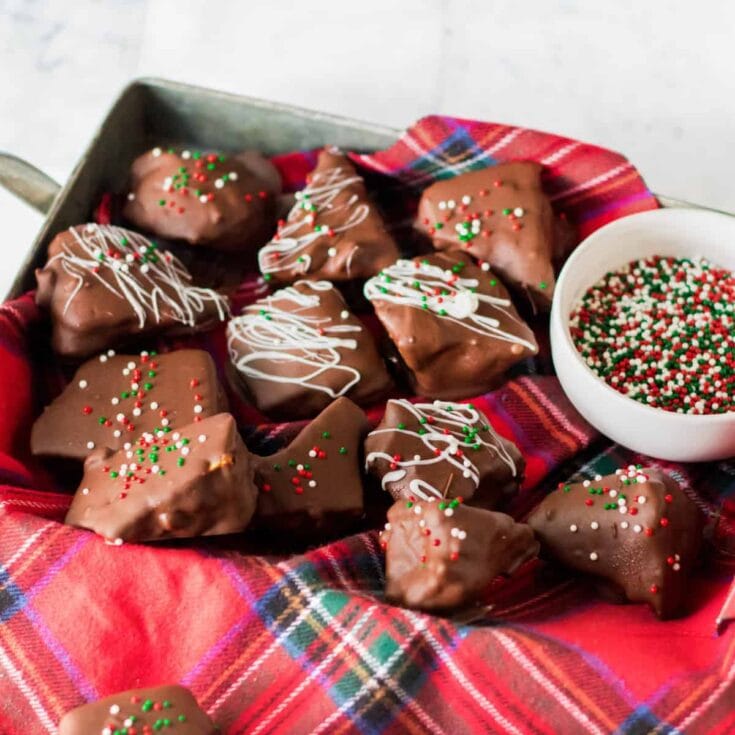 Chocolate chip cookies decorated with colorful sprinkles and white drizzle, placed on a festive red plaid cloth with a bowl of holiday sprinkles nearby. Perfect for holiday baking and Christmas treats.