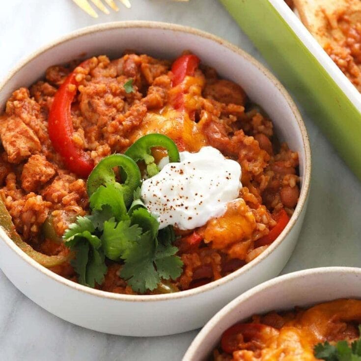 Ground beef chili with red and green peppers, topped with sour cream and cilantro in a white bowl.
