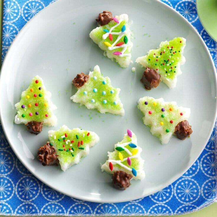 Colorful Christmas tree sugar cookies with festive sprinkles, green icing, and chocolate accents on a light blue plate, perfect for holiday celebrations and decorating.