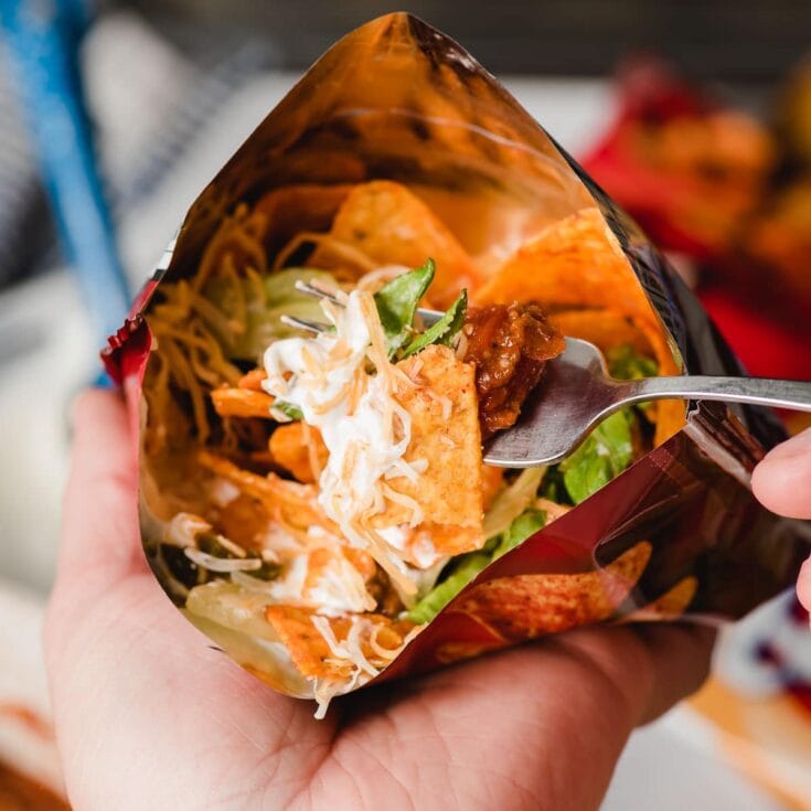Cheeseburger in a bag, with shredded cheese, lettuce, tomato, and sauce, held in hand for a quick and tasty on-the-go meal.
