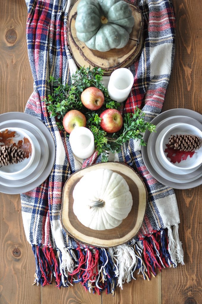 Pumpkin autumn centerpiece with apples, pinecones, candles, and greenery on a rustic table setting for fall decor.