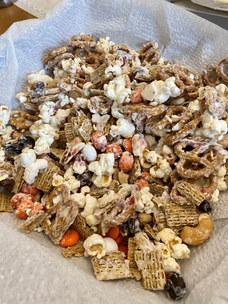 Buttered popcorn and trail mix with pretzels, chocolates, and dried fruit on parchment paper for snacking, emphasizing homemade, sweet, and savory treat options.