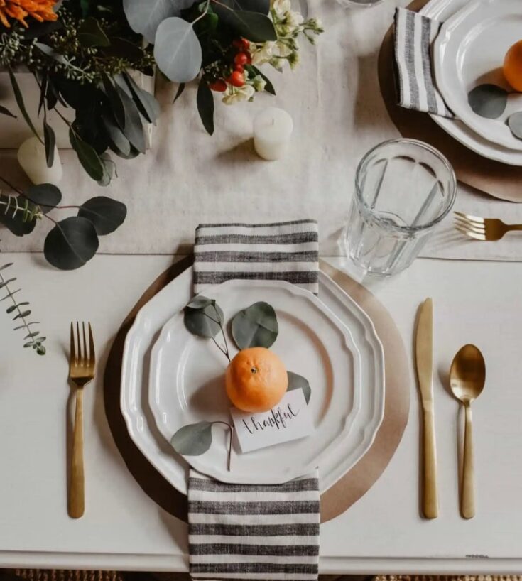 Fresh orange centerpiece on elegant table setting with eucalyptus leaves, gratitude note, and modern gold flatware for holiday or special occasion dinner.
