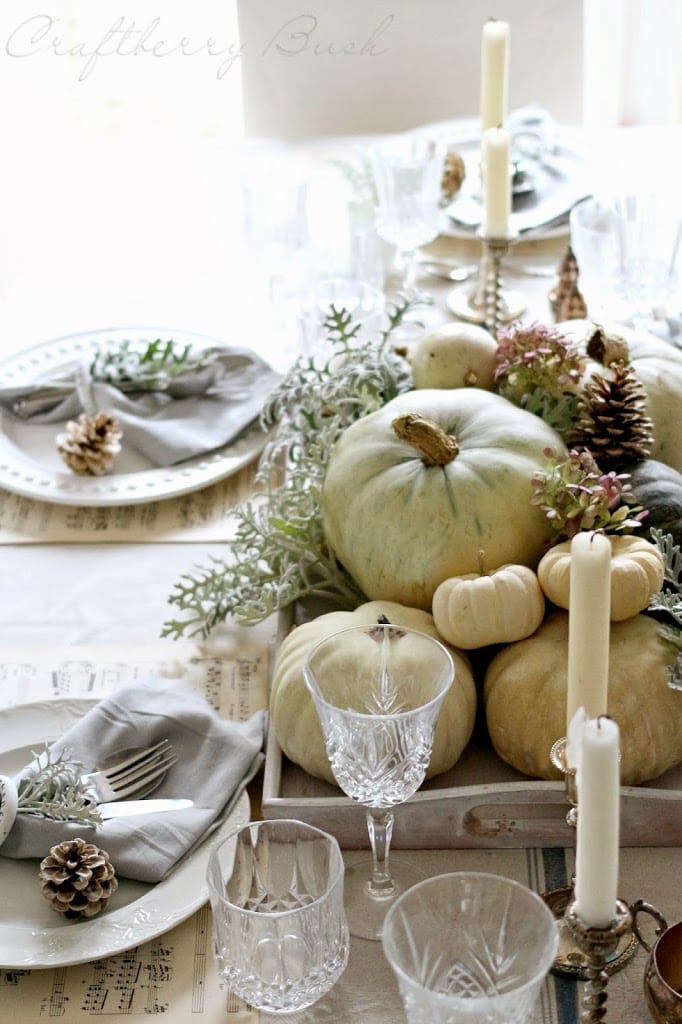 Rustic fall Thanksgiving table centerpiece with white pumpkins, candles, greenery, and pinecones, perfect for holiday decoration and seasonal table setting.