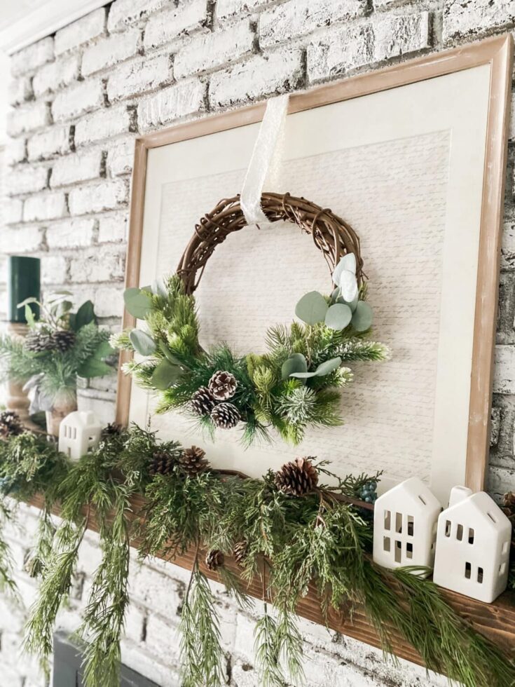 Elegant Christmas wreath with pinecones, eucalyptus, and evergreen foliage hanging on a white brick wall for festive home decor.