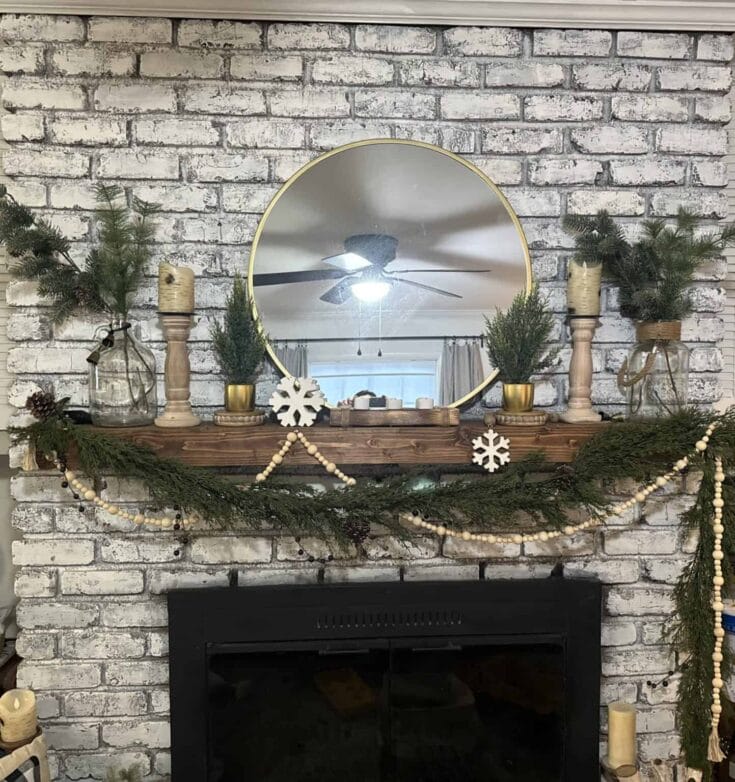 A cozy holiday fireplace mantel decorated with greenery, candles, and rustic wooden accents for Christmas.