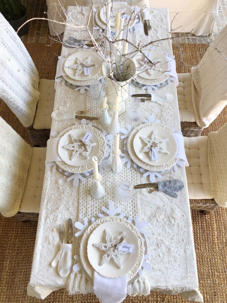 A festive winter-themed table featuring white plates, starfish embellishments, candles, and cozy linens for a charming holiday meal.