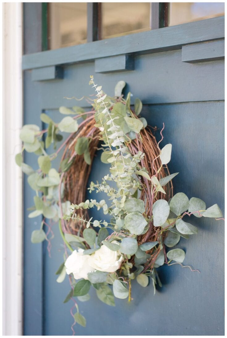 Delicate eucalyptus wreath with white roses hanging on a pastel blue door, perfect for rustic or romantic home decor, wedding decor, or elegant outdoor celebrations.