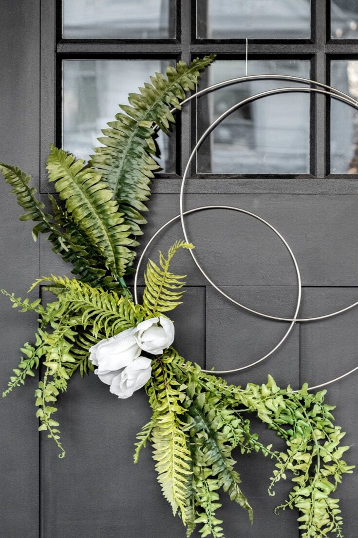 Lush greenery arrangement with ferns, a white flower, and modern metal circles hanging on a dark wall, ideal for home decor or floral styling.