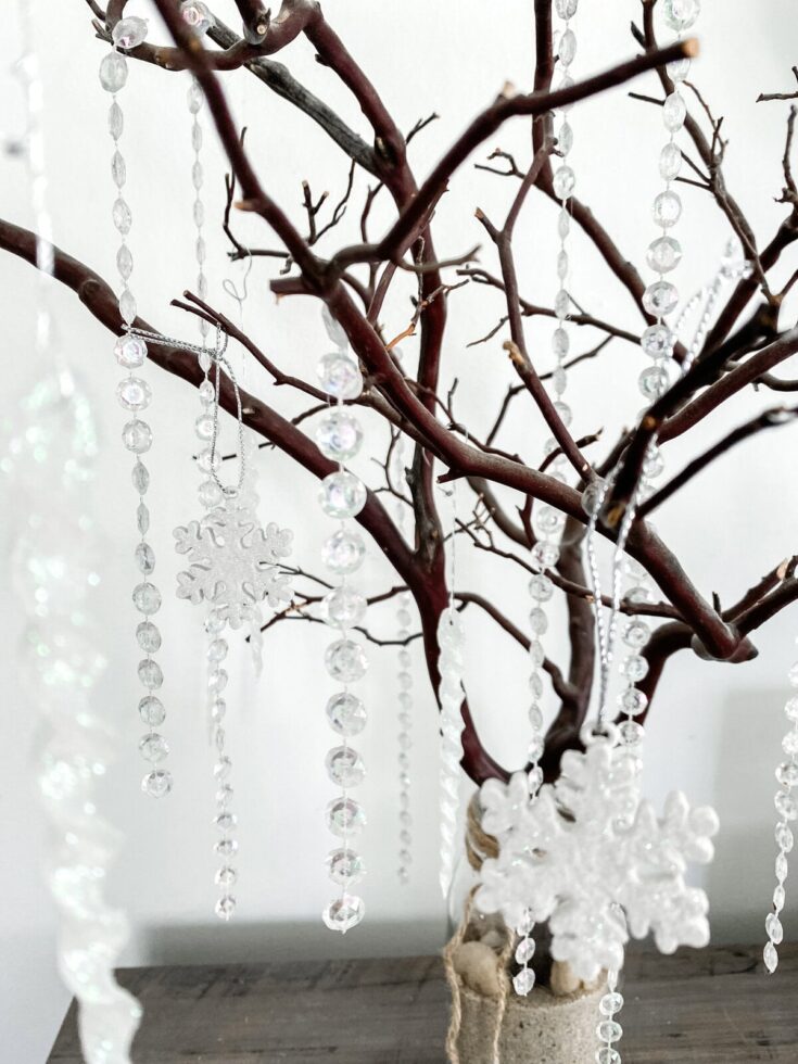 Delicate crystal snowflake ornaments hanging on a dark bare tree branch for winter or holiday decor, creating a sparkling and elegant display.