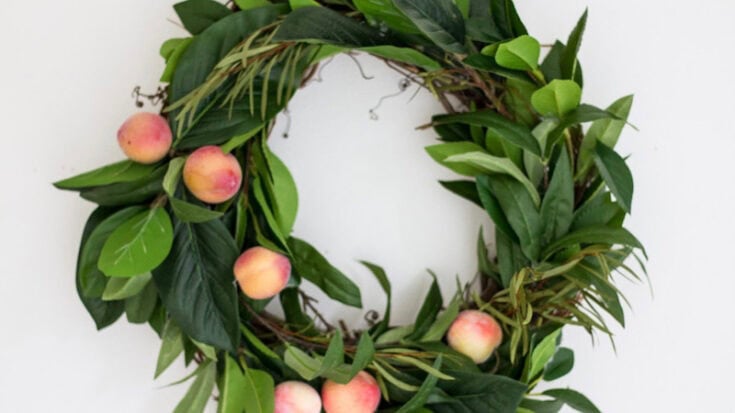 Peach and green leaf wreath on white wall, natural garden decor, lush greenery with fresh peaches for handcrafted wreaths and floral arrangements.
