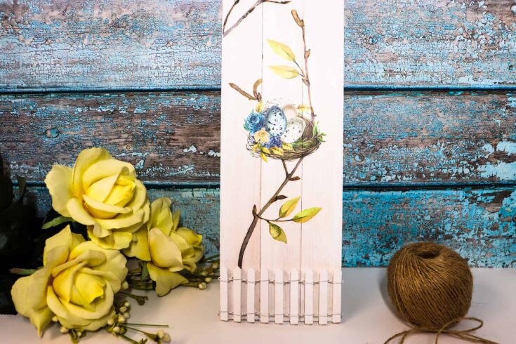 Delicate yellow roses with a wooden mailbox featuring blue eggs and floral accents, set against rustic, weathered blue paint background, perfect for spring or Easter home decor.