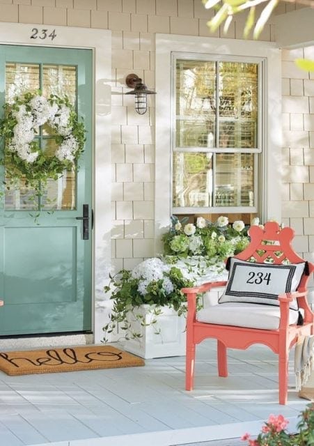 Colorful mint green front door with a floral wreath, inviting porch decor including white flowers and a charming pink bench, perfect for a cozy home entryway.