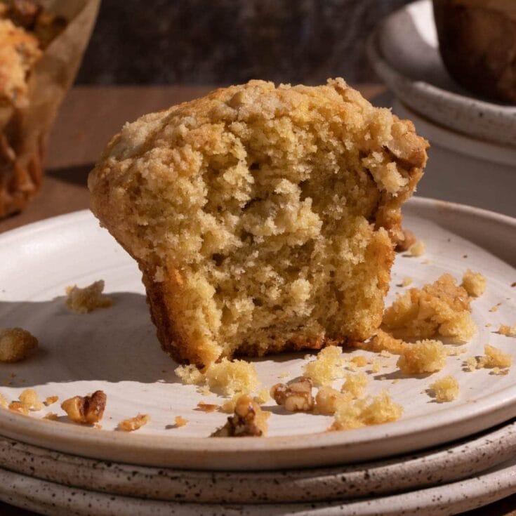 Buttered freshly baked walnut crumb cake on white plate, close-up view for cozy dessert or homemade baking recipe, warm color tones, rustic background, inviting and delicious food presentation.