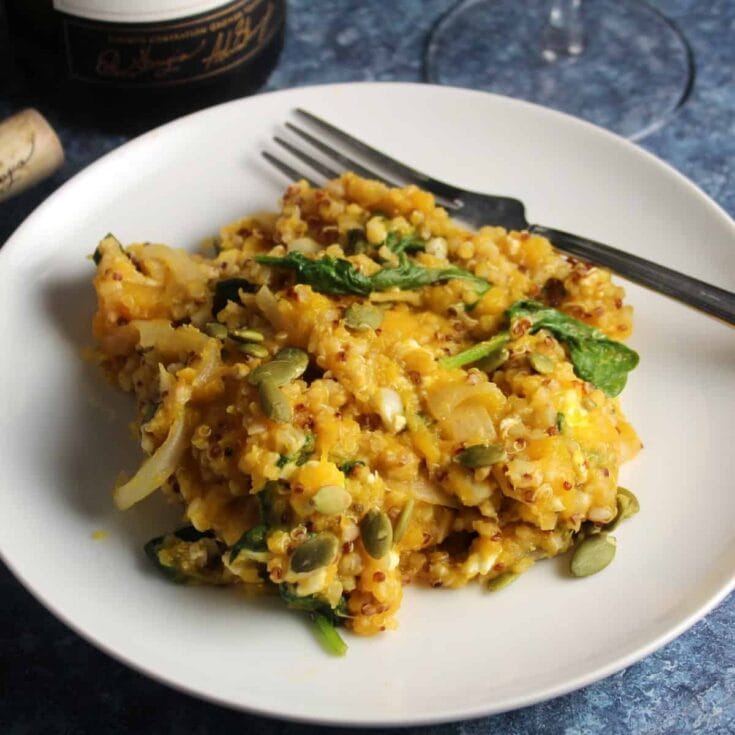 Creamy cauliflower and quinoa casserole with spinach and pumpkin seeds on a white plate, served with a fork. Perfect for healthy, gluten-free dinner options, featuring fresh ingredients and rich flavors.