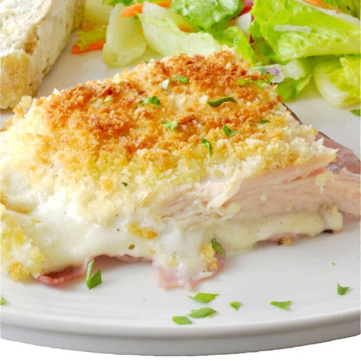 Baked chicken casserole with crispy breadcrumb topping served with fresh salad greens and bread on a white plate.