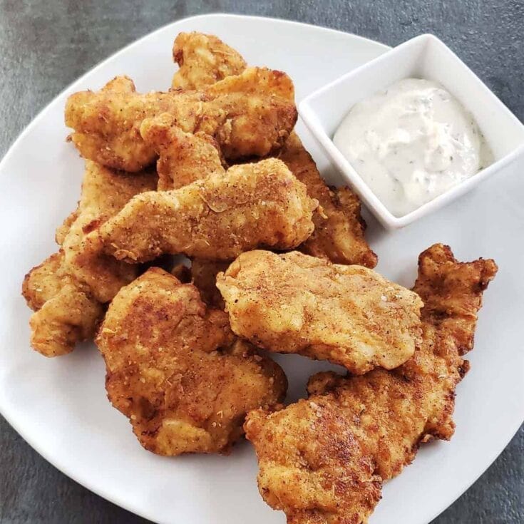 Crispy fried chicken tenders with creamy dipping sauce on white plate, comfort food, Southern-style fried chicken, homemade seasoning, lunch or dinner, savory crispy chicken bites.