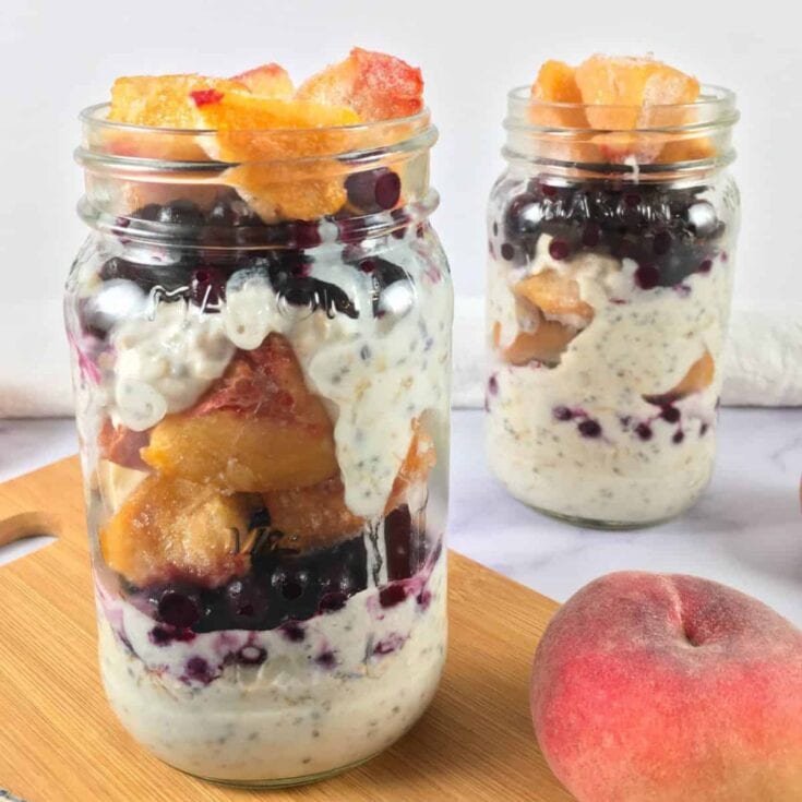 Sweet peach and blueberry parfait in mason jars with fresh fruit and creamy layers, perfect for healthy dessert recipes or summer snacks.