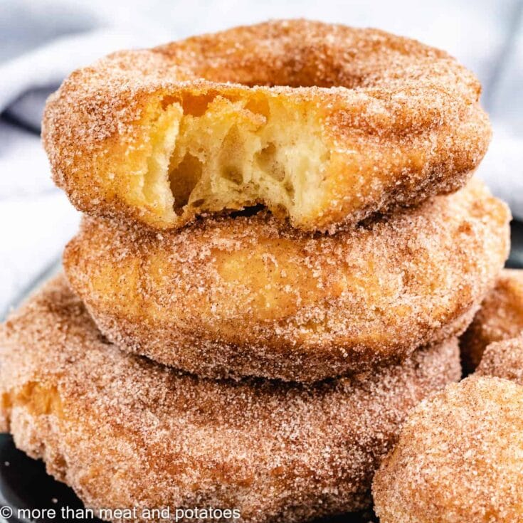 Fluffy, golden brown homemade apple cinnamon donut holes coated with cinnamon sugar, with one donut showing a bite to reveal a soft, moist apple-filled interior. Perfect for breakfast or snack.