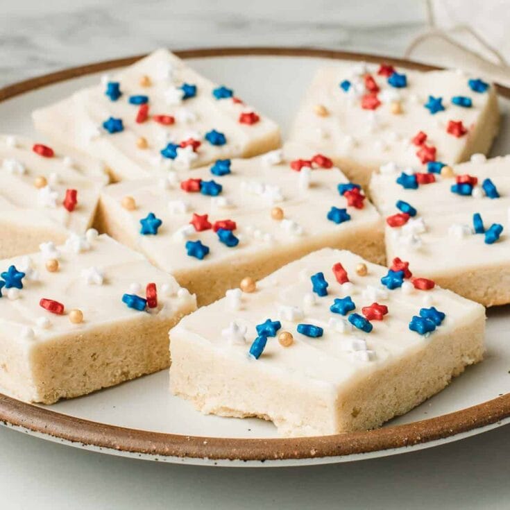 Bright white Valentine-inspired sugar cookies decorated with colorful red, white, blue, and gold sprinkles on a rustic ceramic plate, perfect for holiday celebrations and festive dessert tables.