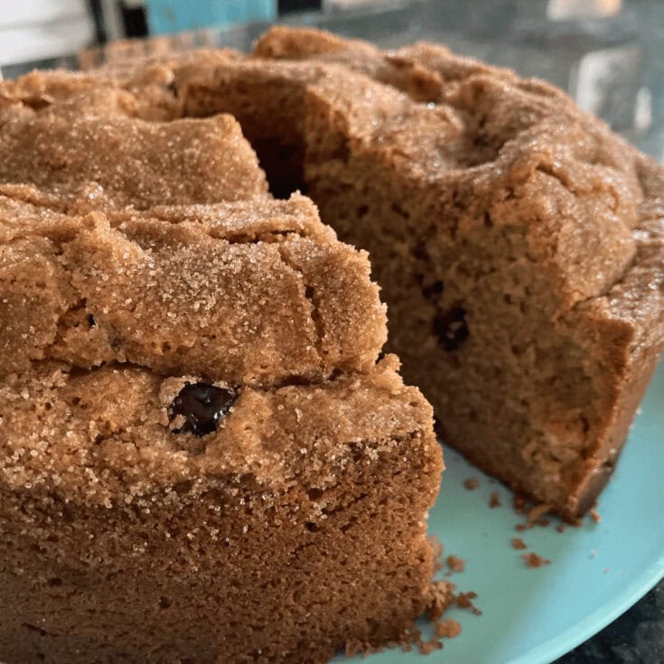 Close-up of a chocolate chip cookie cake with a slice removed, showing the soft interior and chocolate chips, on a blue plate.