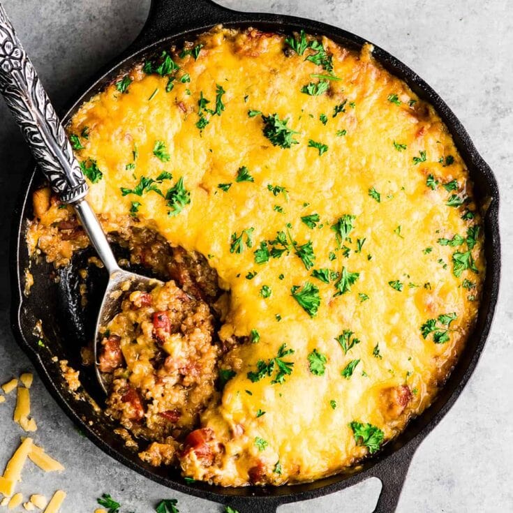 Creamy baked casserole with melted cheese, seasoned ground beef, and fresh parsley garnish, served in a cast iron skillet.