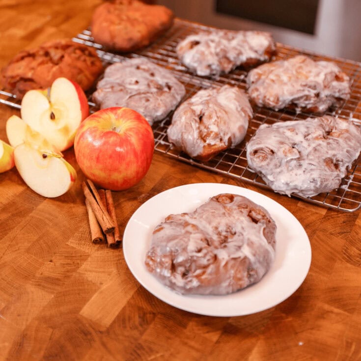 Delicious cinnamon rolls cooling on a wire rack with fresh apples, cinnamon sticks, and a plate of a baked cinnamon roll on a wooden table, perfect for breakfast or dessert.