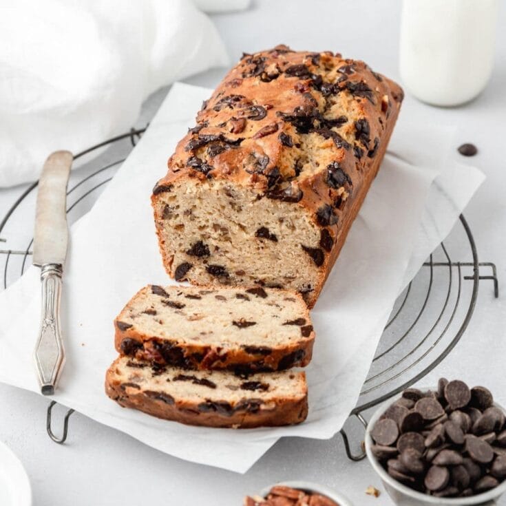Moist chocolate chip banana bread with chocolate chips on top, sliced and placed on white parchment paper, served on a wire cooling rack, perfect for breakfast or snack, from A Hundred Affections.