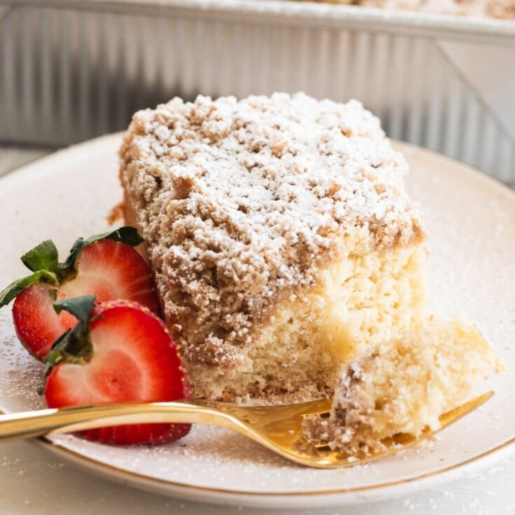 Delicious homemade strawberry crumb cake dusted with powdered sugar, served with fresh strawberries on a white plate, perfect for dessert or afternoon tea.