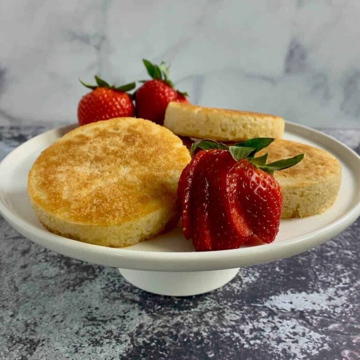 Rich, golden-brown strawberry shortcake biscuits on a white pedestal dish with fresh strawberries and a strawberry slice, styled for a delicious dessert, perfect for breakfast or brunch, highlighting homemade baked goods and fresh fruit ingredients.
