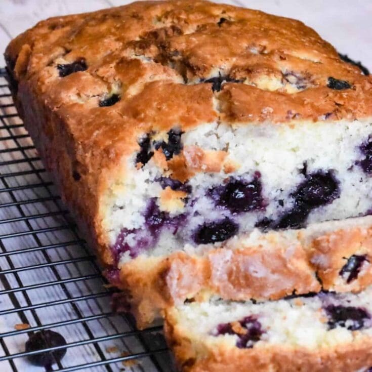 Blueberry crumb cake drizzled with glaze, freshly baked and cooling on a wire rack. Perfect for breakfast or an afternoon treat, highlighting moist cake texture and ripe blueberries.