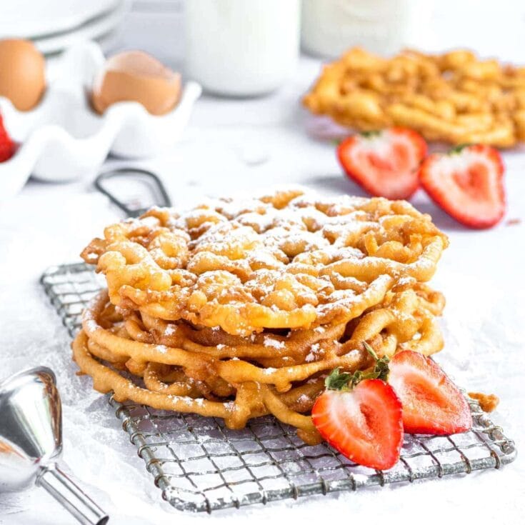 Crispy funnel cake with powdered sugar and fresh strawberries on a cooling rack, delicious breakfast or dessert option, homemade funnel cake, street food classic, sweet and crunchy treat, summer fair food.