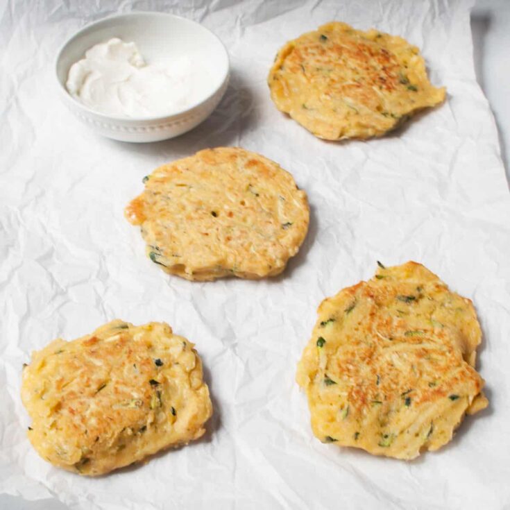 Fluffy zucchini fritters served with a side of creamy yogurt sauce on crinkled parchment paper. Perfect for healthy breakfast or snack options. Fresh zucchini and herbs make these fritters flavorful and moist.