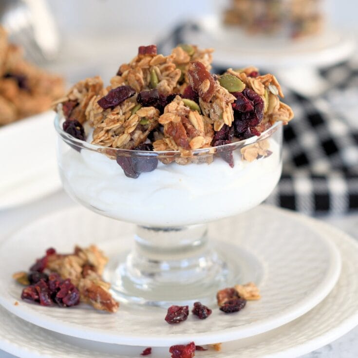 Crunchy granola and dried berry parfait in a glass dessert cup, topped with yogurt and served on an elegant white plate. Perfect for a healthy breakfast or snack.