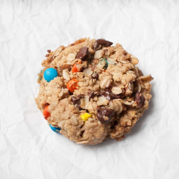 Chewy oatmeal chocolate chip cookie with colorful candy-coated chocolates on crumpled white parchment paper background. Perfect for chocolate lovers and cookie connoisseurs.
