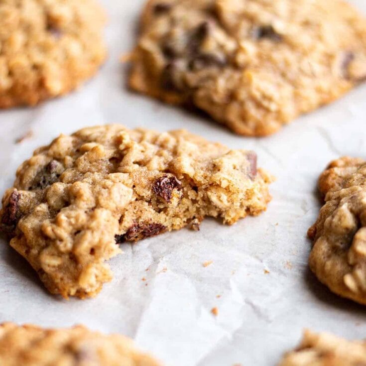 Buttery oatmeal chocolate chip cookies with a golden-brown color, loaded with chocolate chips, fresh out of the oven, on white parchment paper, showcasing soft and chewy texture, perfect for homemade baked goods, comforting treats, classic cookie recipe.