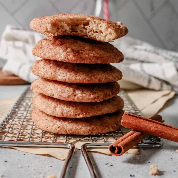 Butter cinnamon cookies stacked on a wire rack with cinnamon sticks in the foreground.