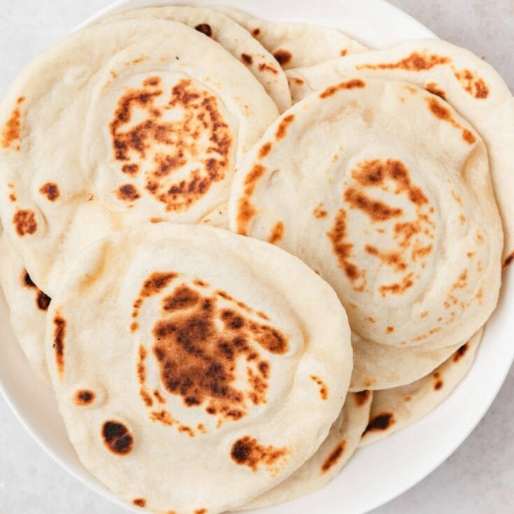 Soft, freshly cooked naan bread with golden-brown spots, served on a white plate, ideal for sharing and enjoying with various dishes.