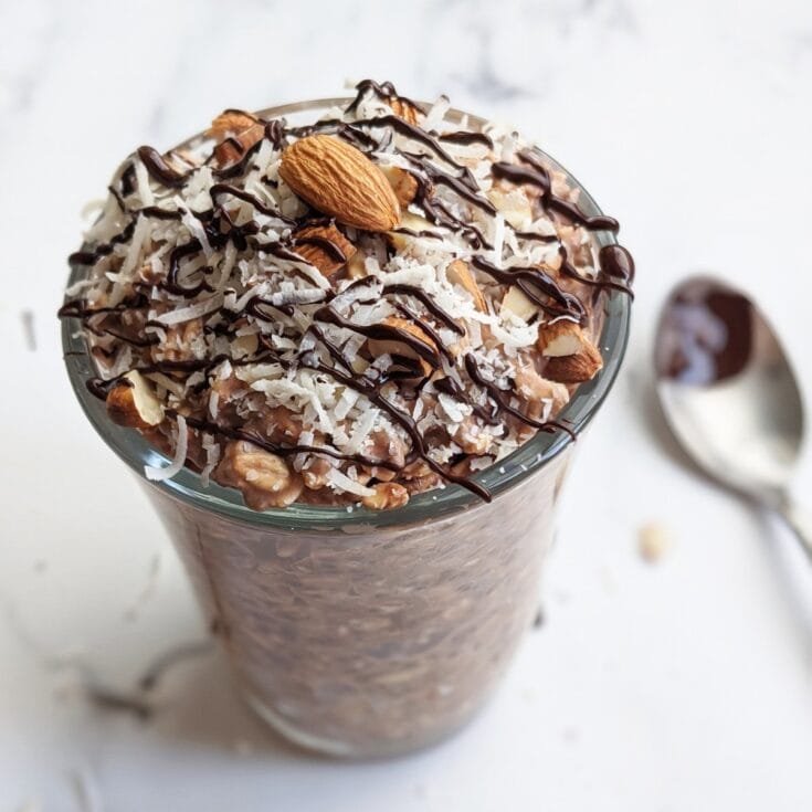 Rich chocolate oatmeal almond yogurt parfait topped with shredded coconut, chopped almonds, and drizzled with chocolate sauce for a healthy, indulgent breakfast or snack.