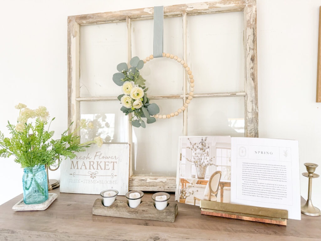 cottage spring vignette with vintage window pane, fresh market flowers sign, cozy seasons liz marie galvin book in book holder, blue mason jar with faux florals, candle holders