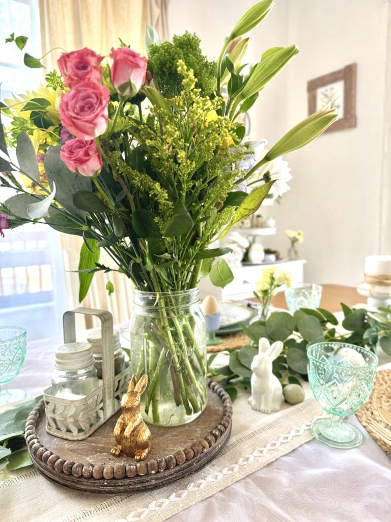 Vibrant spring flower arrangement with pink roses, white lilies, and greenery in a glass vase on a decorated table, perfect for Easter or springtime celebrations.