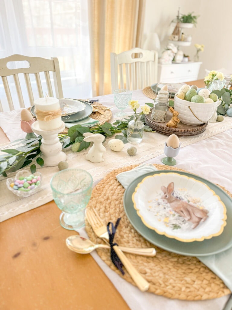 Pastel Easter table setting with spring-themed decorations, bunny-shaped ornaments, and decorated eggs for festive celebration, featuring soft colors and elegant details.