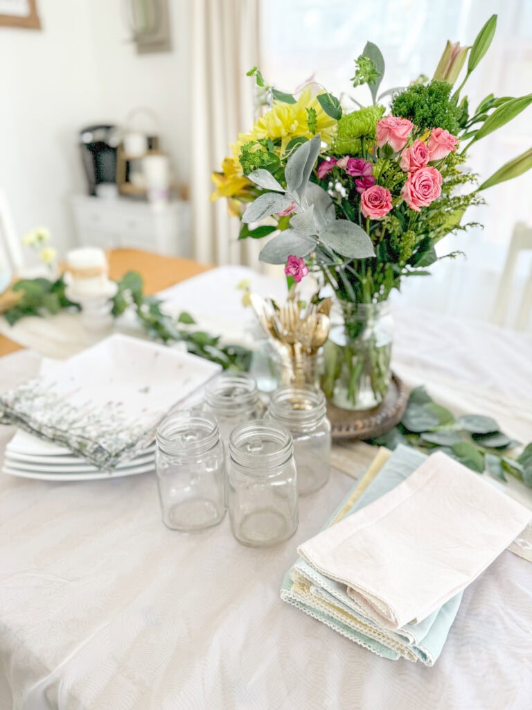 spring centerpiece of fresh floral flowers with square white ceramic plates, mason jar glasses, wildflower and pastel linen napkins