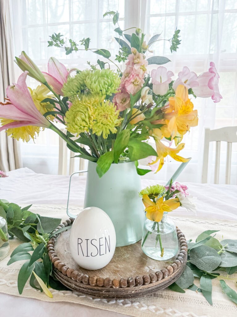 Easter table with risen egg and bud vase, flowers in watering can centerpiece