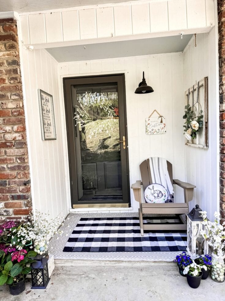 Cozy house entrance decorated for Easter with flowers, a striped mat, and a rocking chair, highlighting charming outdoor decor and springtime holiday spirit.