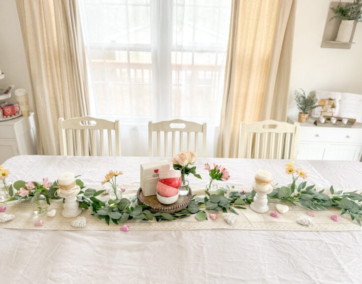 Soft candle decor, pink roses, greenery, and heart-themed accents on a rustic dining table create a romantic and elegant setting for special occasions or intimate gatherings.