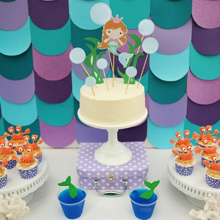 Colorful under-the-sea mermaid birthday cake with themed snacks and decorations, perfect for a children's party. Featuring mermaid topper, ocean-themed cupcakes, and vibrant decor for a whimsical celebration.